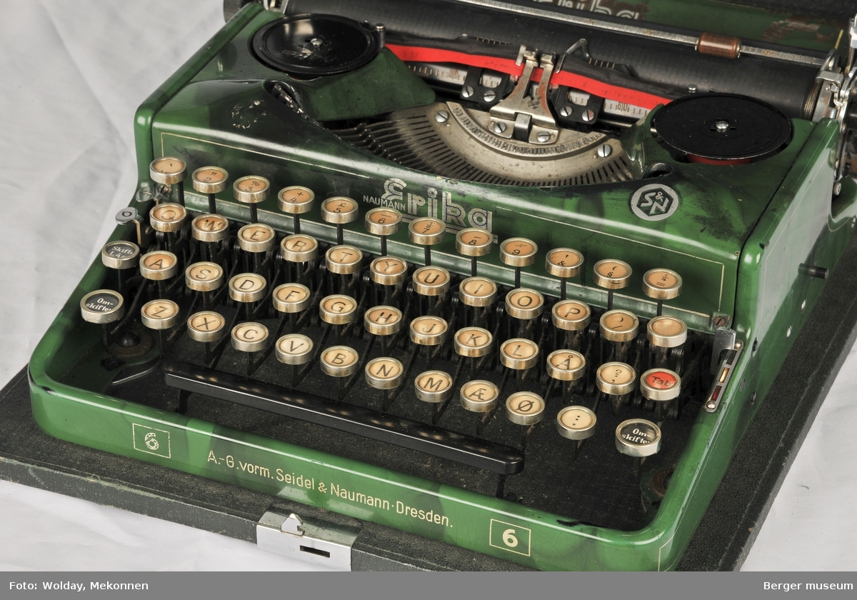 Reisekoffert med skrivemaskin. Skrivemaskinen er festet til koffertens nedre del og den har et avtagbart og låsbart lokk. Kofferten kan låses og det medfølger nøkkel. Innunder lokket er det festet en pensel til å rengjøre skrivemaskinen med.