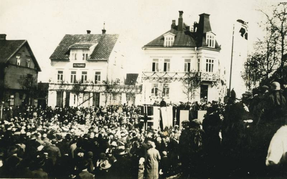 Folkemengde foran festpyntede hus. Musikere på scene pyntet ,ed flagg. Narvik feirer 25-års byjubileum i 1926.
Rådhuset til h, Astrupgården nederst til v.