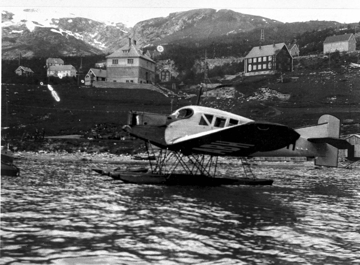 1 fly, Junkers F13 LN-ABH (N-44) fra Nord-Norges Aero A/S, Narvik, på havet fortøyd ved strandkanten. Noen bygninger i bakgrunnen