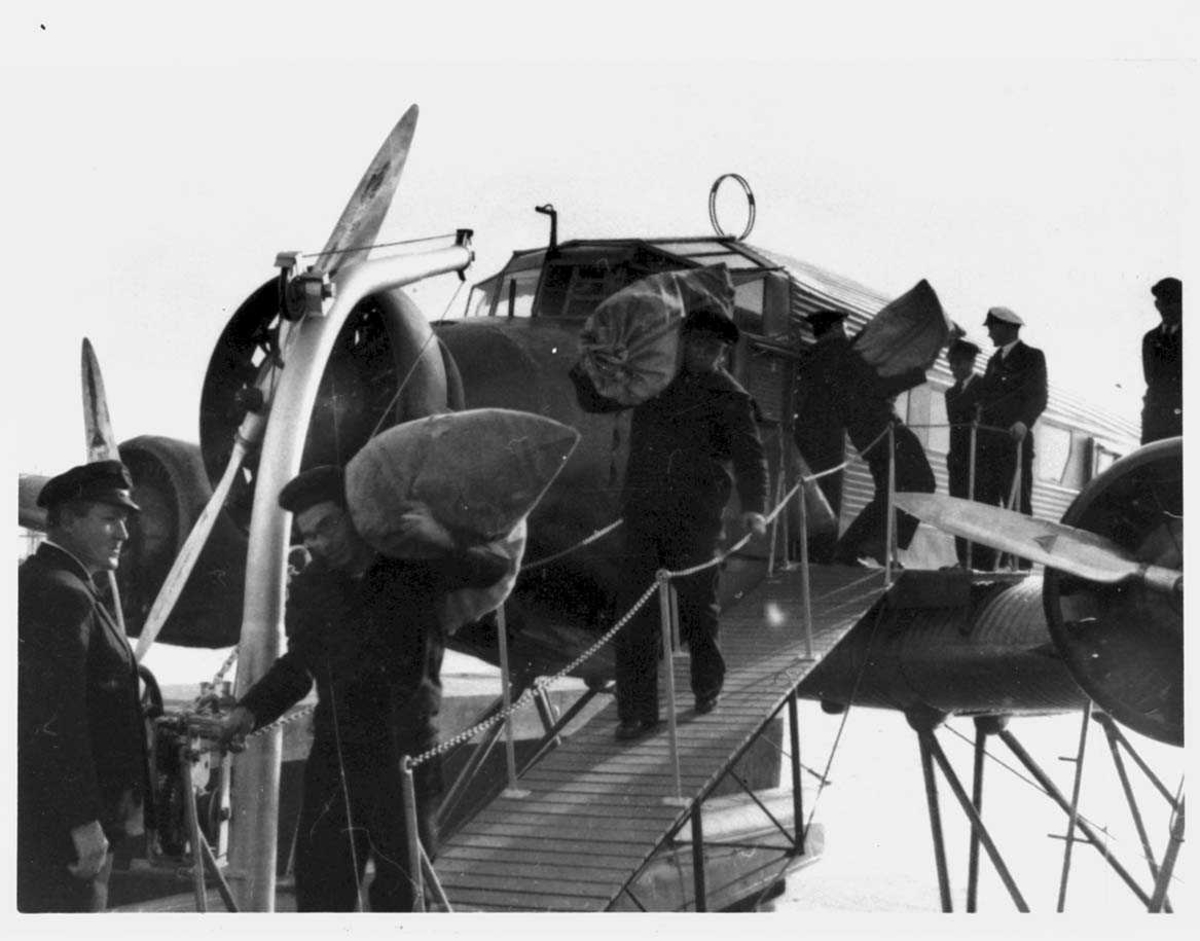Ett fly på havet. Junkers Ju52. Flere personer med sekker ved flyet.