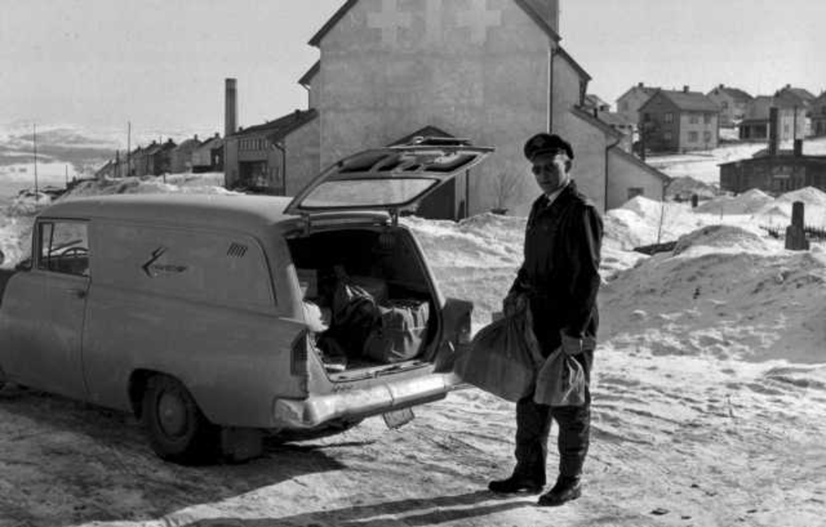 En person, mann, i flygeruniform laster post inn i et kjøretøy, Opel Olympia varebil 1958-60. Snø på bakken.