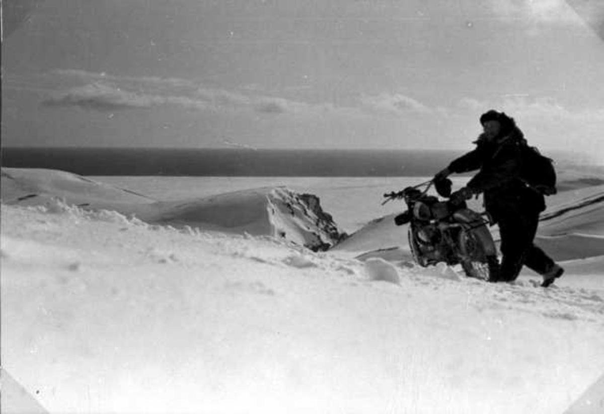 En person, mann, med en motorsykkel. Snø på bakken.