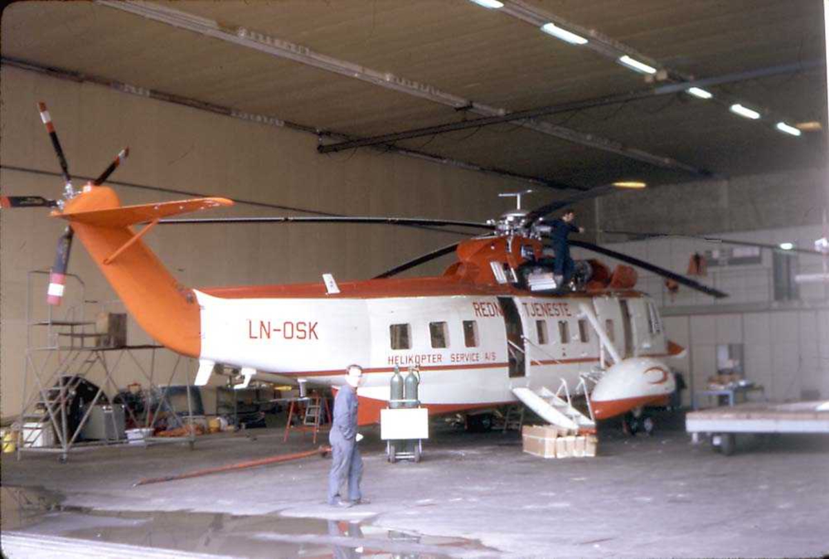 Ett helikopter inne i en hangar. Sikorsky S-61N Mk II, LN-OSK fra Helikopter Service. En person står foran helikoptret. 