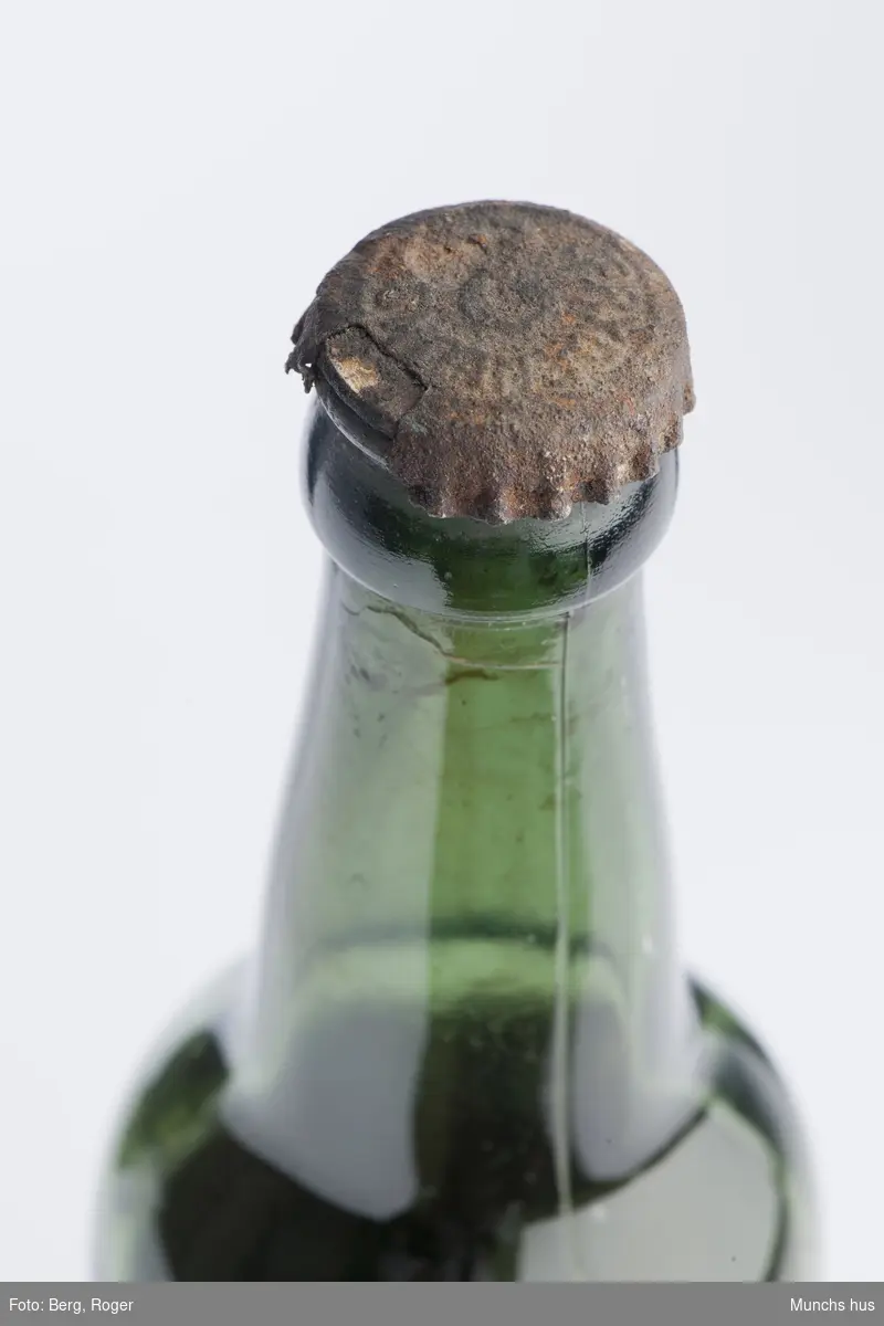 Ølflaske i grønt glass. Med kork. med innhold, antakelig øl.
Tekst på kork: Frydenlund.