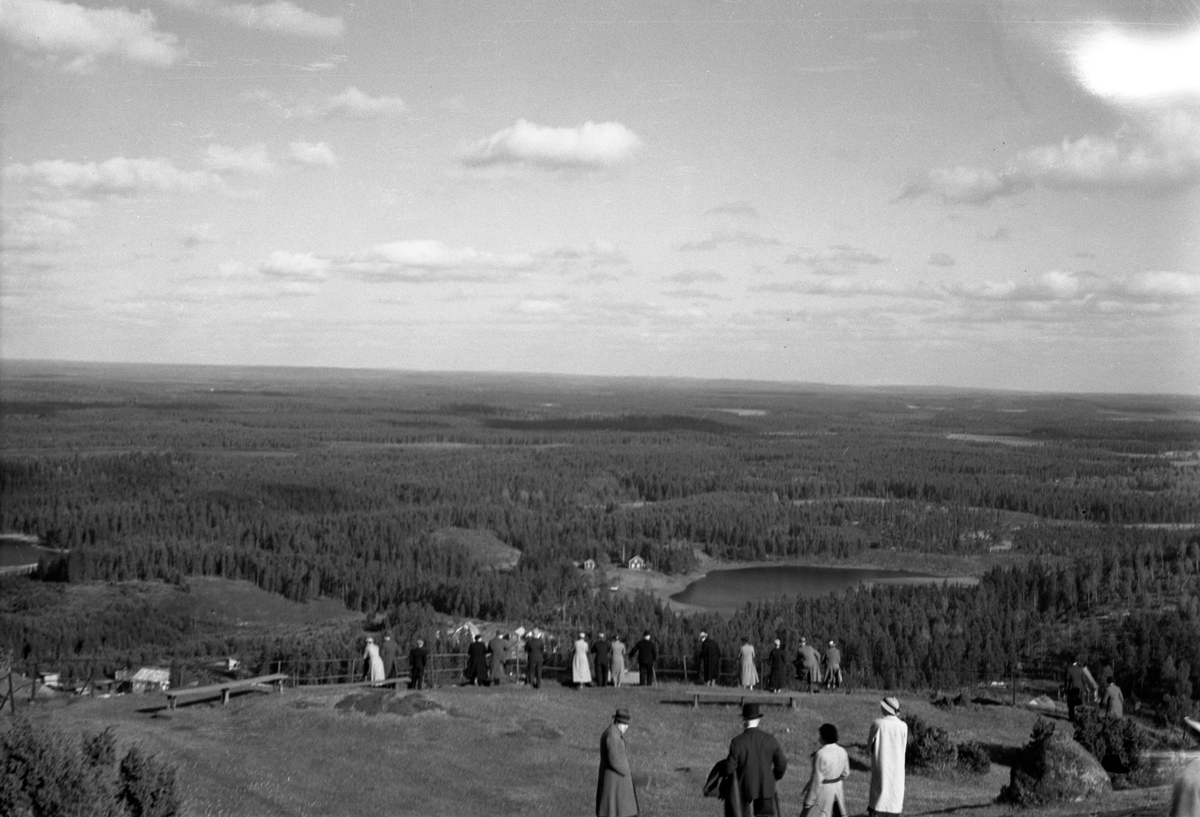 Människor tittar på utsikten från Tabergs topp. Utsikt över Nordgårdsgölen, (Skarmaden) i Månsarps socken, Jönköping.