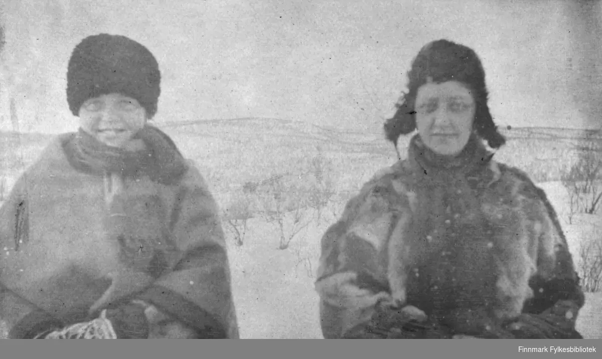 To kvinner fotografert i vinterlige omgivelser i Tana. Begge er kledd i pesk, og har både skjerf, lue og votter på