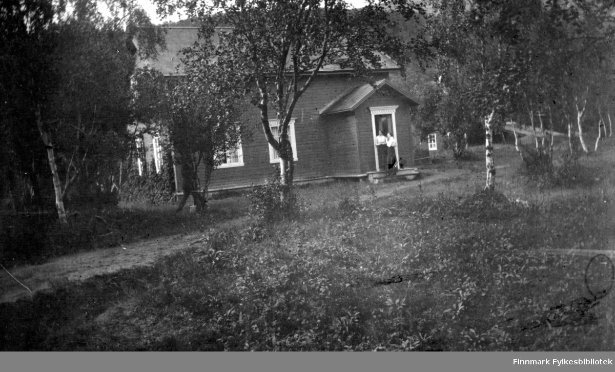 To damer står på trappen til et hus i Rasjok i Tana. I bakgrunnen kan man skimte et uthus og en låvebru.