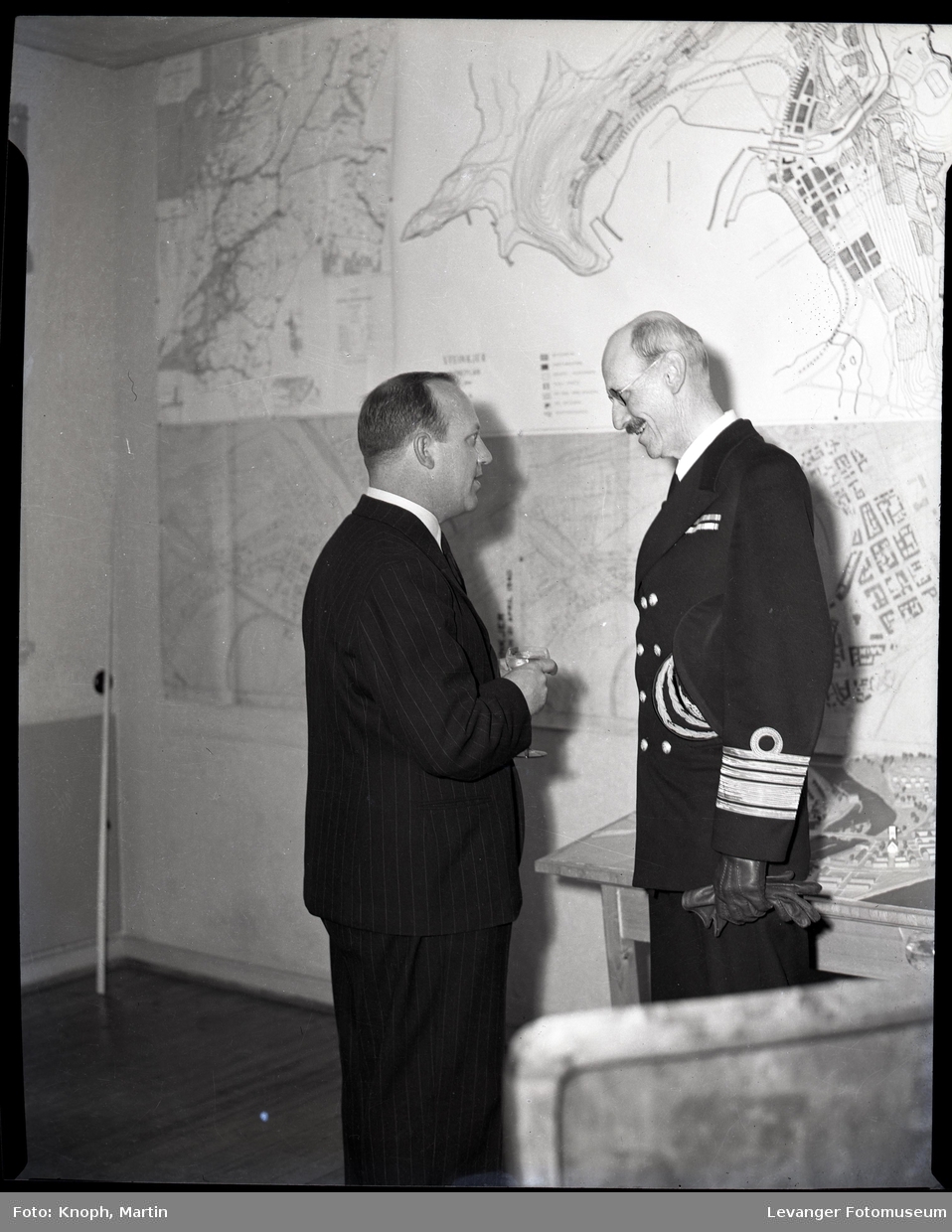 Kong Haakon med  kart og modell over Steinkjer, i samband med gjernreisningen i Steinkjer etter at byen ble bombet.