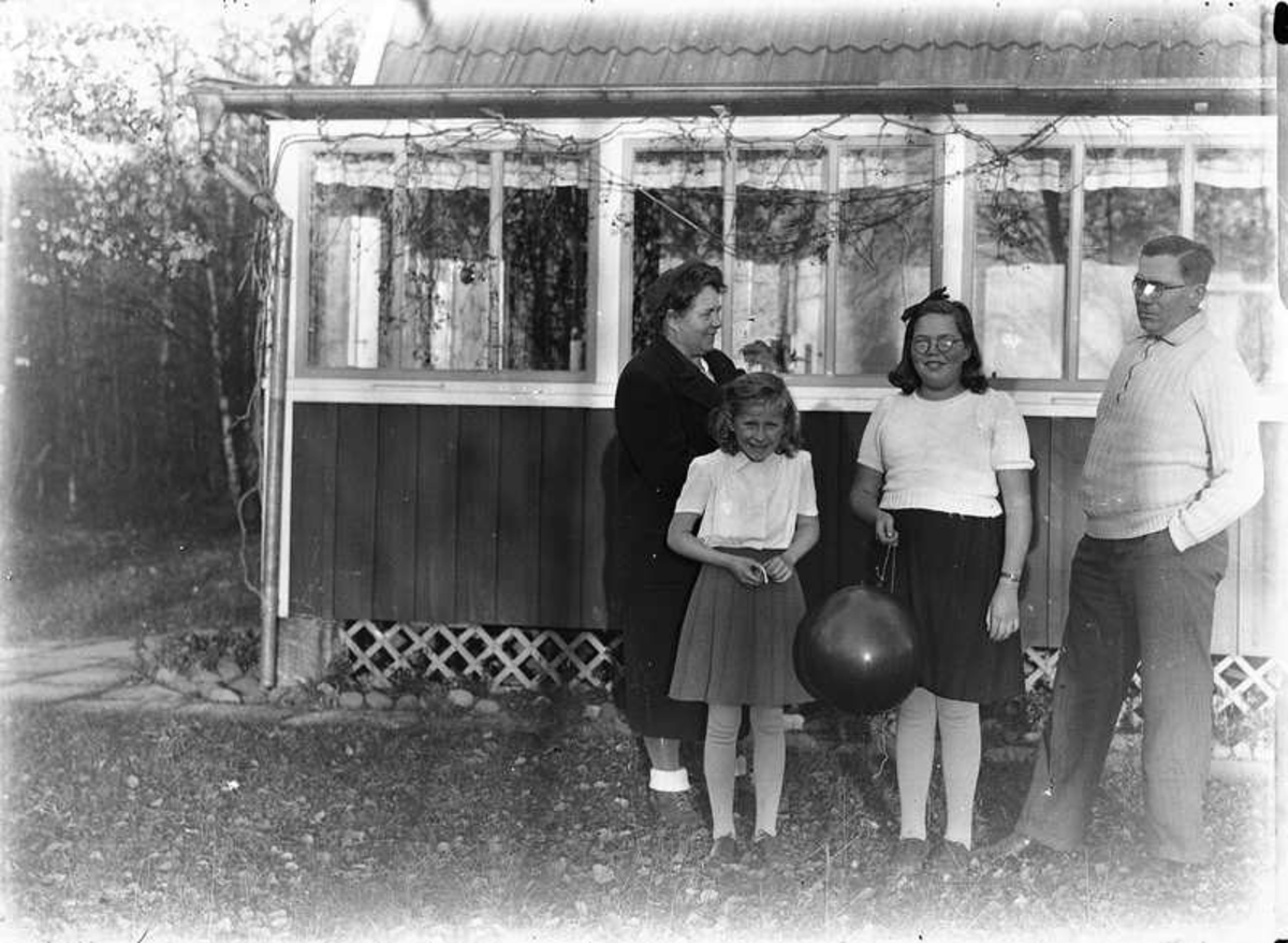 Familj vid liten stuga. Sannolikt är det fotografen själv t.h. framför stugan vid Nordkroken, Vargön.