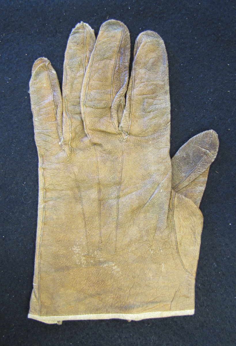En brun skinnhandske, små kilar mellan fingrarna Knapp och knapphål vid handleden.

Se VM 08 710