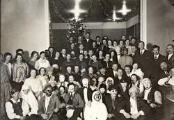 Gruppebilde av kvinner og menn foran juletre. Flere personer