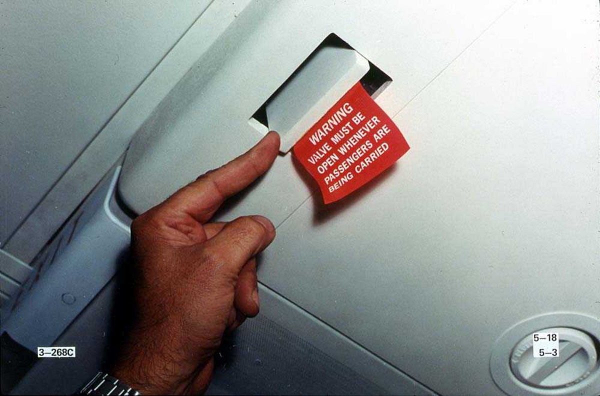 En person som peker på en luke hvor det henger en merkelapp på, inne i en Boeing 737-200.