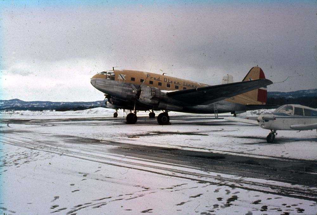 Lufthavn. Ett fly på bakken, Curties C-46R Commando LN-FOR fra Fred Olsen Flyveselskap. Et annet fly ved siden av. Snø på bakken.