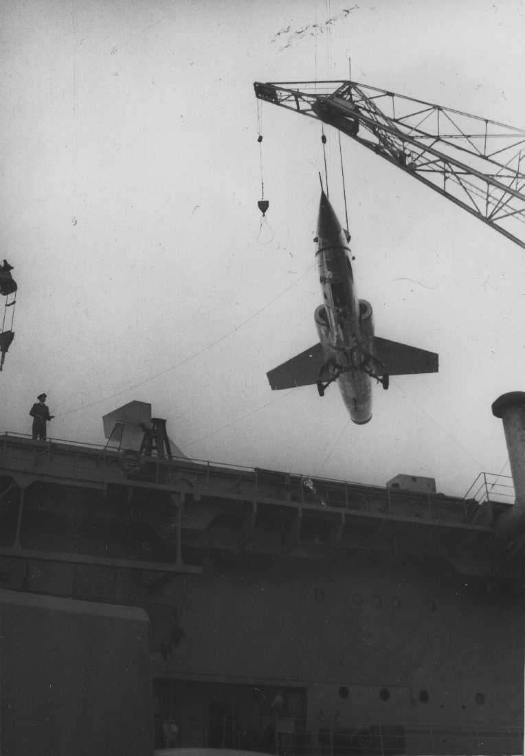 Båt - Marinefartøy. Ett fly, F-104 Starfighter henger i en heisekran.
Flyet heises fra et fartøy 
