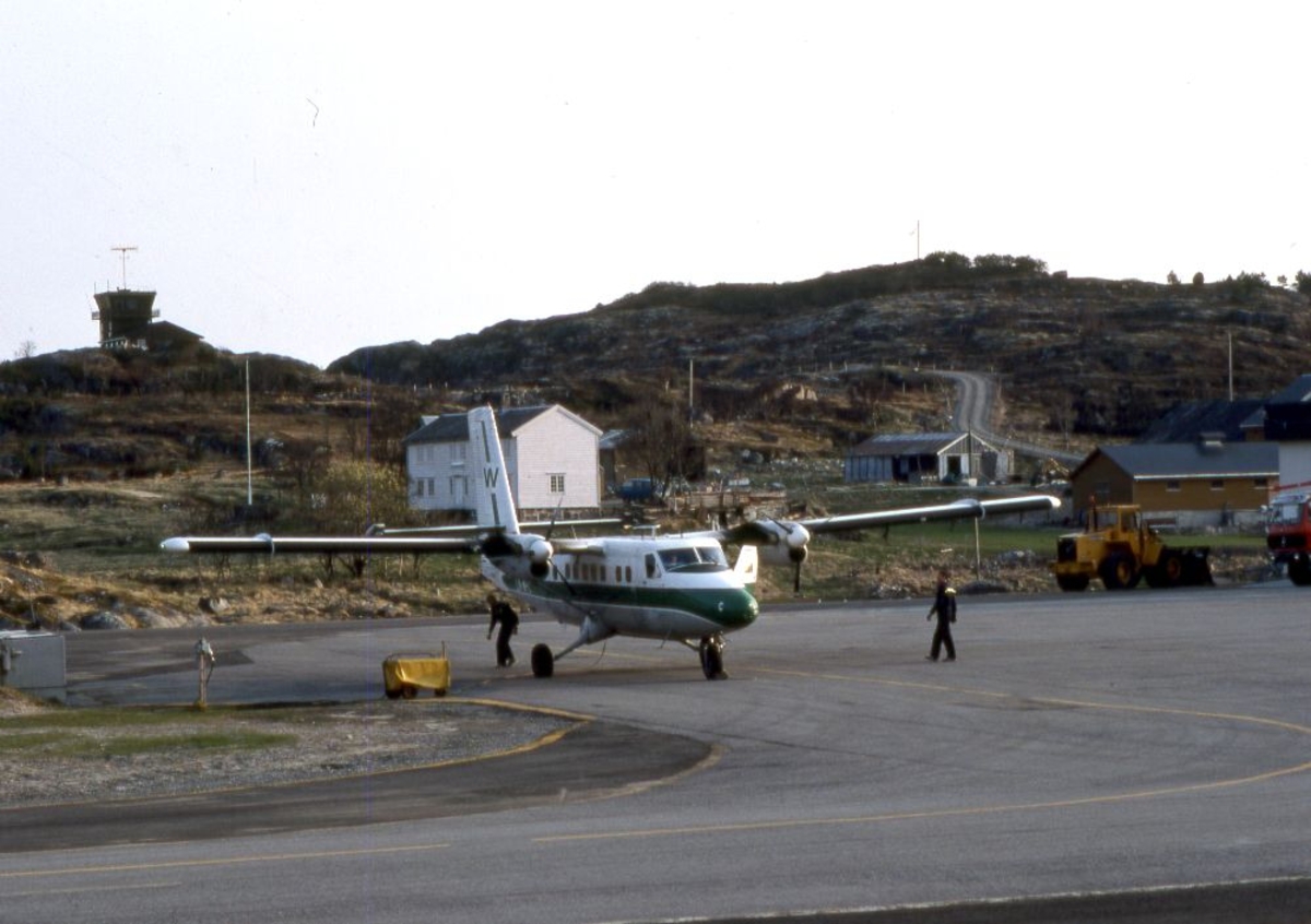 Lufthavn (flyplass). Et fly, LN-WFC, DHC-6-300 Twin Otter fra Widerøe parkert. To personer klargjør flyet for avgang. På en høyde i bakgrunn ligger Flytårnet.
