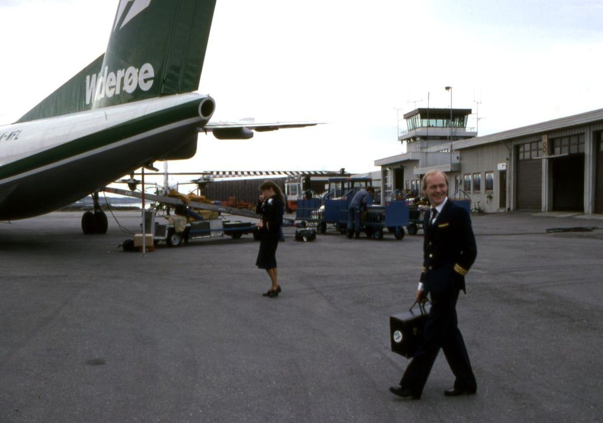 Lufthavn (flyplass). Halepartiet på et fly, LN-WFL, DHC-7-102 Dash 7 fra Widerøe. To personer, pilot (flyger) og kabinansatt underveis til flyet. I bakgrunn Flytårnet.