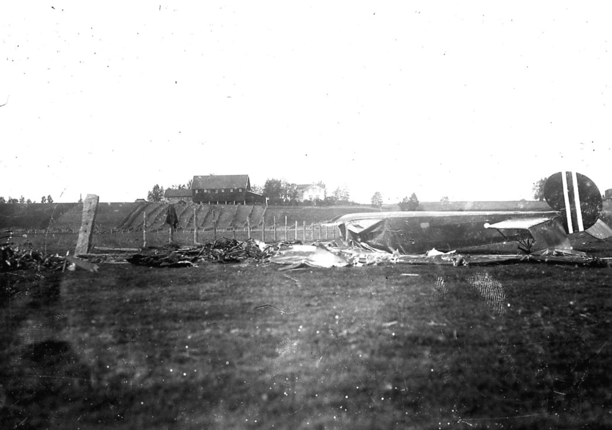 Flyvrak/flykrasj. Avro 504 nr. 107, ligger i mange biter på bakken etter havari. ett gårdsbruk bak.