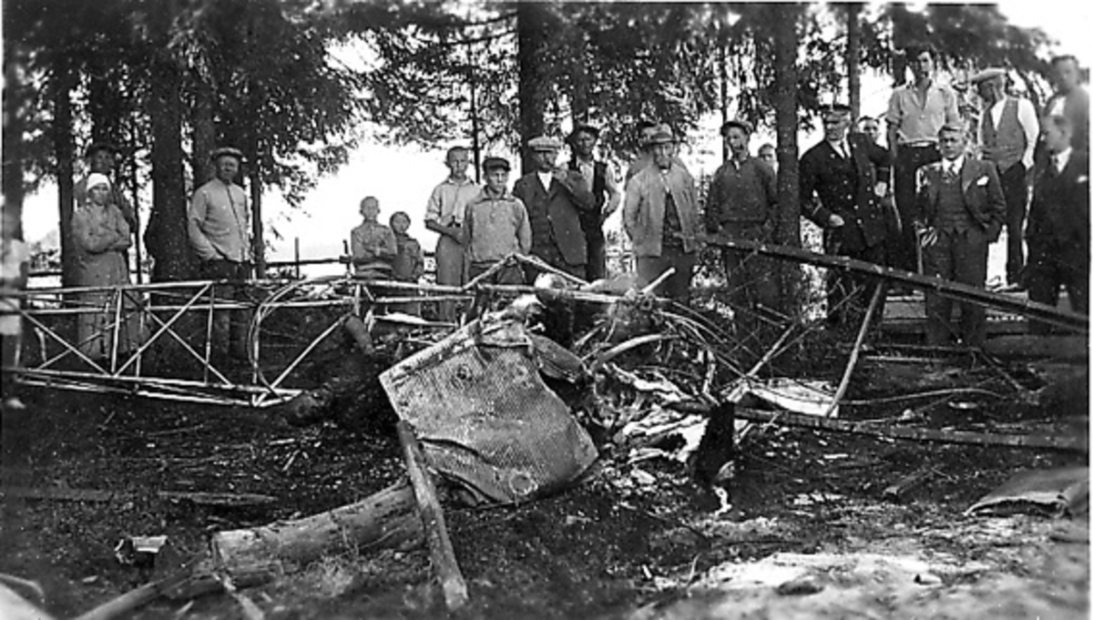 Flyhavari, flyvrak. Totalt ødelagt fly. Flere personer i bakgrunnen. Noen trær.