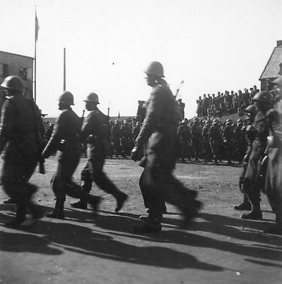 Frigjøringsdagene i Bodø etter krigen  1945. Mange soldater marsjerer ved kaiområdet. Sylinderformet "tank" bak med mange personer oppå.