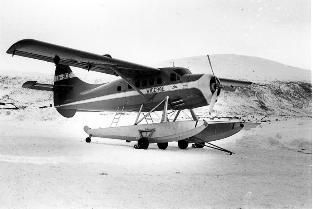 Ett fly på flotører, med hjul under. LN-BDD, De Havilland, Canada, DHC.3 Otter.cn 138 fra Widerøe AS.  Står på land. Snø på bakken.