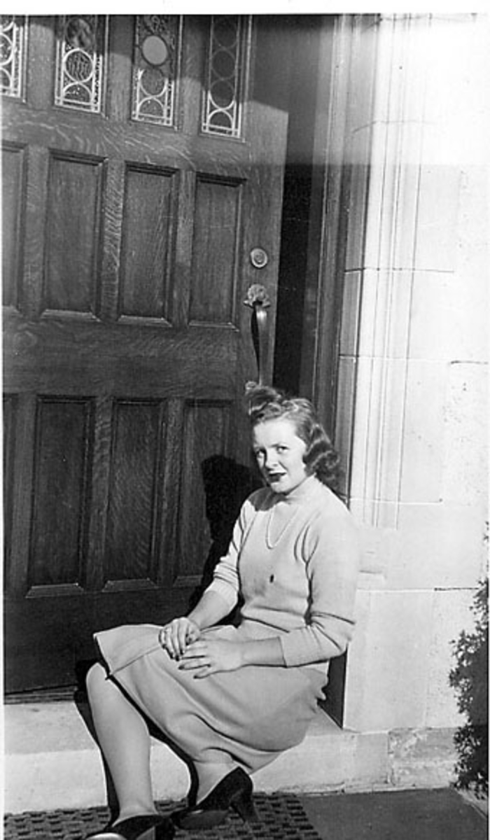 Portrett, en person sitter på trappa foran inngangen til ei bygning. Ung kvinne i sivile klær. 