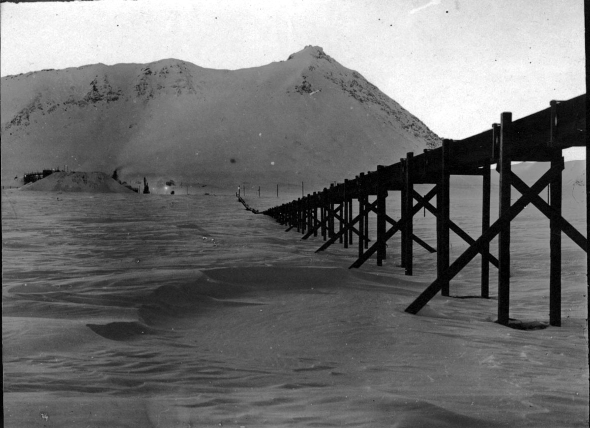 Jernbanelinja til gruvene i Ny Ålesund. Bygd på peler. Snø på bakken, fjell bak