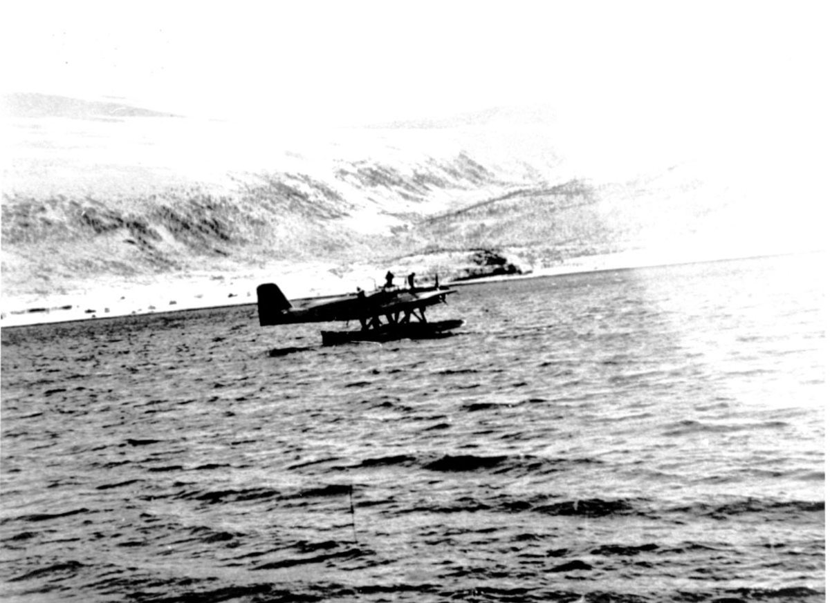 Sjøfly, propellfly, ute på fjorden. 2 personer står på flyskroget ...