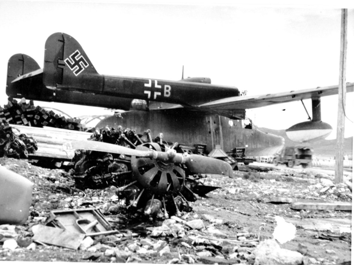 Fly, propellfly, med "hakekors. Flydeler, vrakdeler i forgrunnen. En lastebil i bakgrunnen.
Blom und Voss BV-138