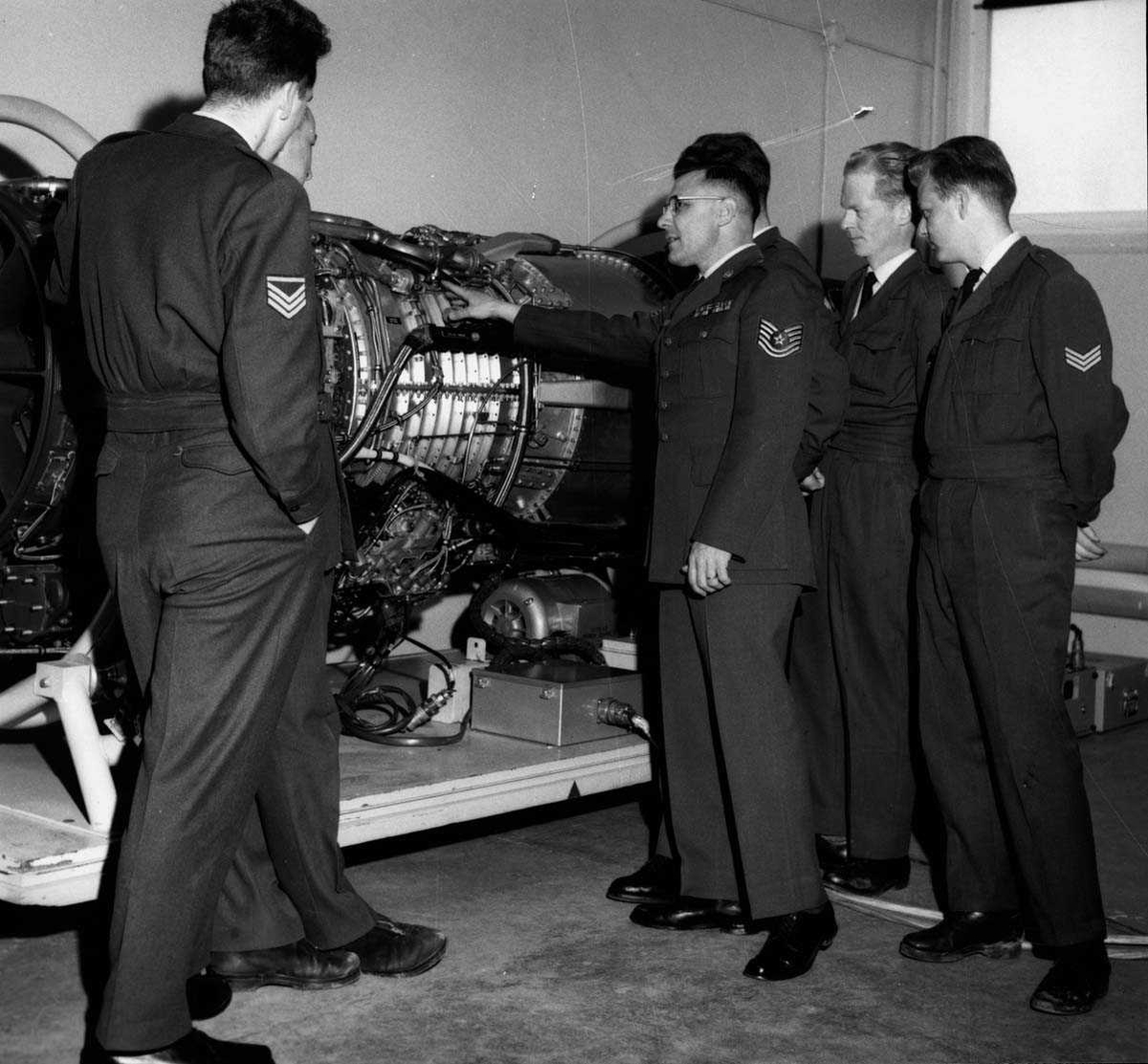 Gruppe.  Seks personer i uniform ved siden av en jetmotor.