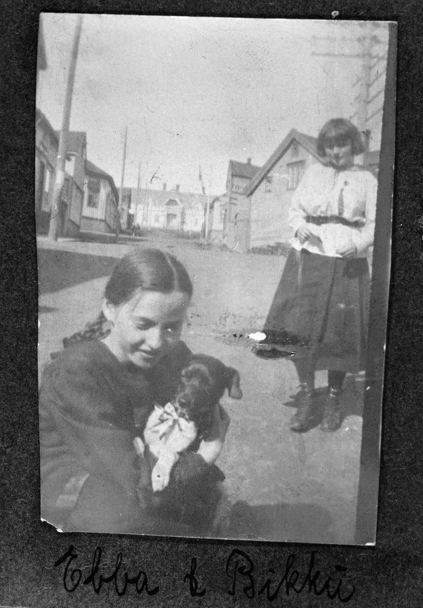 Ung jente, Ebba, leker med hunden Rikki på gatan trolig i Vadsø. Hunden har sløyfe på seg. Bilder er tatt på sommerhalvåret.