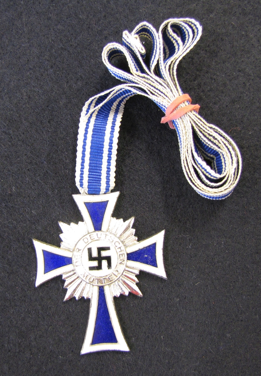 Medalj i silverfärgad metall med blå emalj.  På baksidan finns datumet "16 December 1938" och Adolf Hitlers namnteckning ingraverat. Medaljen är fäst i ett band. Förvaras i originaletui.

Medaljen är "Ehrenkreuz der Deutschen Mutter eller i översättning Hederkorset till den tyska modern. Medaljen kallades även i vardagligt tal för Mutterehrenkreuz eller Mutterkreuz. Medaljen utdelades till en tysk mor för exceptionella meriter till den tyska nationen.

Medaljen instiftades 16 december 1938 av Adolf Hitler och delades ut mellan 1939 och 1945. Kriterier för att få medaljen var att man uppvisat redlighet, exemplariskt moderskap samt att man fött minst fyra barn. Medaljen delades till en början ut på mors dag, andra söndagen i maj. Senare kunde den dock även delas ut på andra högtidsdagar under året.

Det fanns tre klasser av medaljen:
1 klassen, guldkorset, delades ut till mödrar som fött åtta eller fler barn
2 klassen, silverkorset, delades ut till mödrar som fött sex eller sju barn
3 klassen, bronskorset, delades ut till mödrar som fött fyra eller fem barn


Kriterierna för att få utmärkelsen var:

Att båda föräldrarna var av tyskt blod, samt att deras föräldrar i sin tur inte var judiska eller hade annat etniskt ursprung och att de heller inte tillhört någon judisk församling.

Att mamman verkligen var värdig medaljen. Att mamman var hedervärd vad gäller moral samt att hon var genetisk frisk. Hon fick inte ha varit otrogen, gjort abort eller ägnat sig åt prostitution eller haft sexuella relationer med andra raser.

Att barnen inte fick ha några ärftliga eller genetiska sjukdomar. Mannen fick heller inte suttit i fängelse, familjen fick inte vara alkoholister eller ligga samhället till last och vara beroende av varken privat eller social välfärd.

Att inget barn varit döfött.

Medaljen kunde dras tillbaka om modern inte längre bedömdes som värdig, till exempel om hon försummade sina barn, om hon var otrogen inom äktenskapet eller uppvisade andra problematiska beteenden.

Denna medalj delades ut till systern till Greta Hennice (1897-1989). Under första världskriget träffade Greta Hans på ett fältsjukhus och tycke uppstod. De gifte sig och bodde i Tyskland fram till krigsutbrottet. De anade vart det barkade med Tyskland med Hitler vid rodret så de flydde då till Sverige. Efter Andra världskriget då Tyskland delades i Öst och i Väst, hamnade platsen där Gretas syster bodde i Östtyskland.

Greta var gudmor till givarens äldsta dotter.