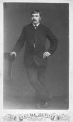 Helportrett av en mann. På bildet står han lent mot en stol.