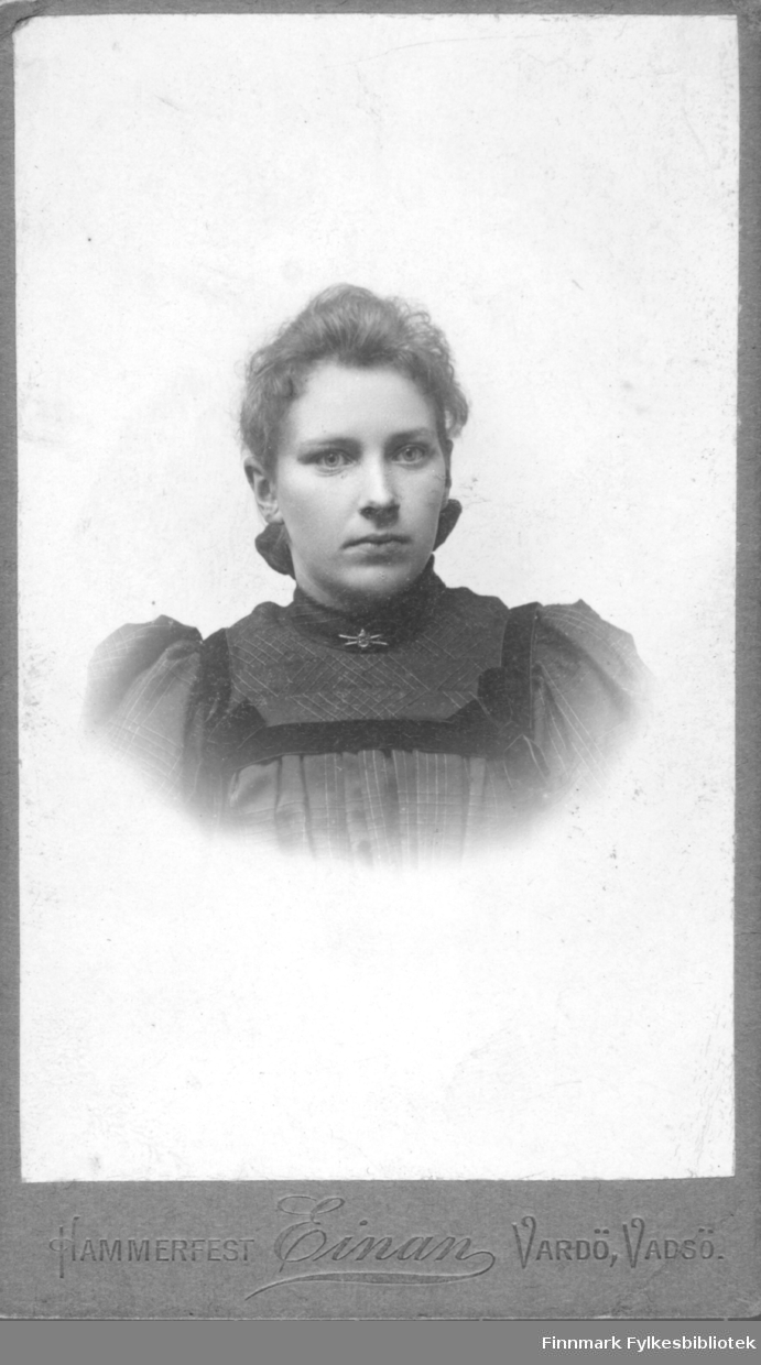 Portrett av en ung ukjent kvinne. Hun er kledt i en mørk kjole eller bluse som er pyntet med fløyelsbånd. I halsen har hun en brosje