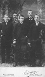 Gruppeportrett av fem menn tatt i et fotoatelier. Mannen til