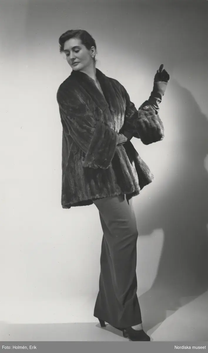 Nordiska Kompaniet. Kvinna i mörk pälsjacka och mörk, lång klänning. Text på baksidan: "Horowitz f. rysk hermelin 1951"