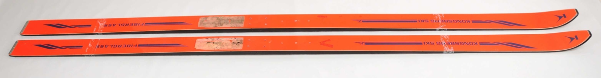 Hoppski laga av glasfiber. Oransje overside, svarte sidekantar Kvit plastsåle med namnet Kongsberg ski synleg gjennom plastbelegget, 6 riller på midten av såla. Metallbeslag på baktuppane. Det er bora hol til bindingar.