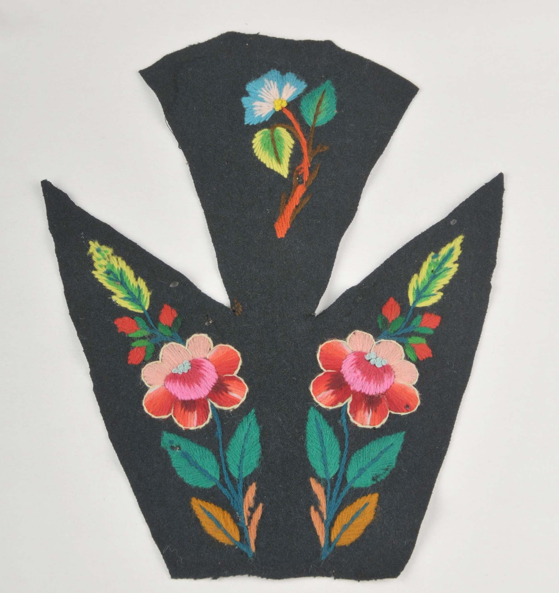 Broderi på svart klede, del av bakstykke til eit draktliv. Motivet er blomar og blad i sterke fargar. Blomene er kanta med kontursting i kvitt. 