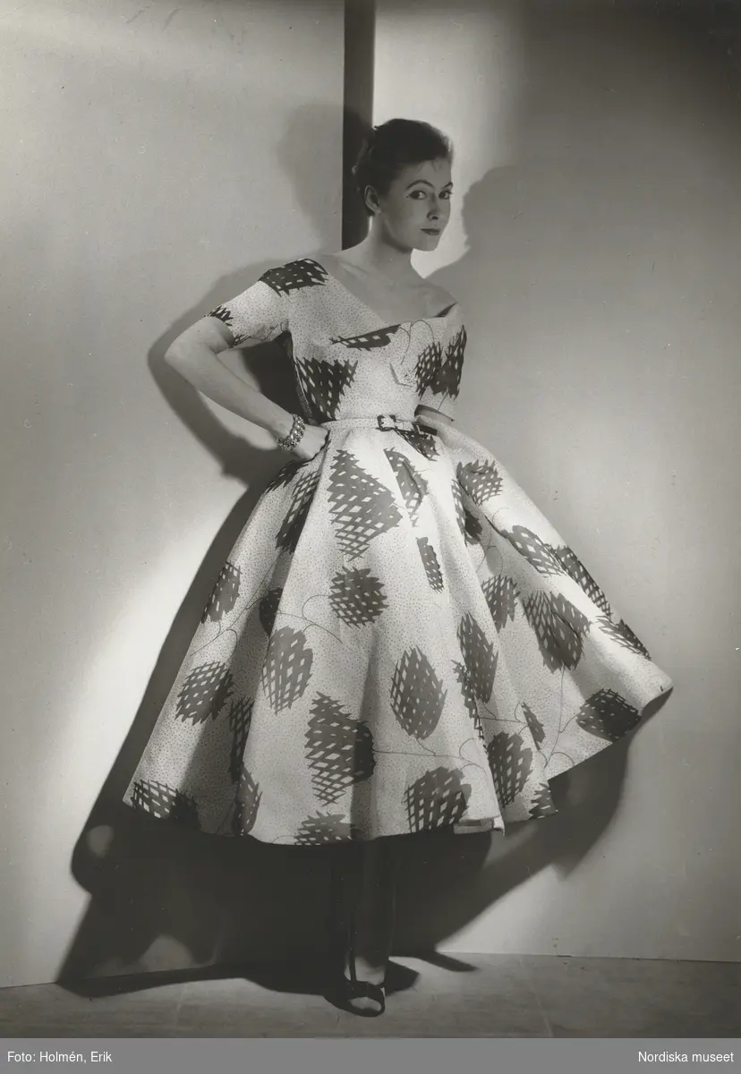 Modell i mönstrad klänning med vid kjol och skärp. Från Jacques Fath.