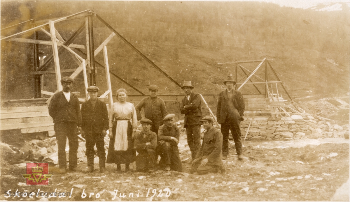 Gamle Skøelvdal bru i Troms,  juni 1920. Arbeidslag og  kokke. Bruanlegget i bakgrunnen. Tekst på bildet: "Skøelvdal bro Juni 1920".