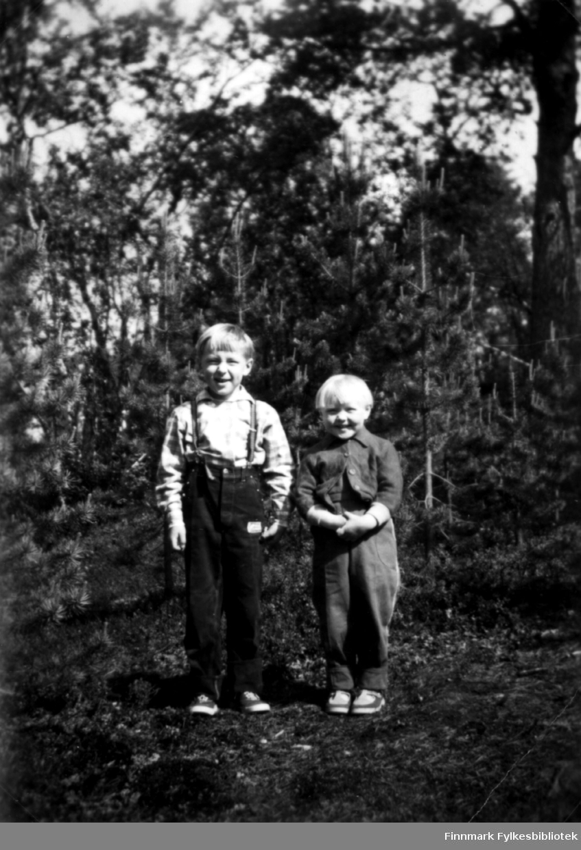 Fotografi av Trygve og Ingrid Stenbakk. På bildet står de ved, eller i en skog. Det er mange trær i bakgrunnen. Begge barna har 'pottefrisyrer'. Trygve er kledt i skjorte og bukser med seler. Ingrid har på seg bukse og jakke. Det ser ut som et sett
