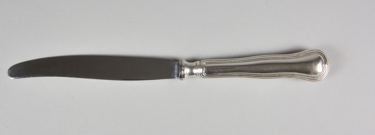 Matkniv av silver med knivblad av stål. På skaftets ovansida löper en kant som i övre änden avslutas i en hjärtformad spets. Med stämplar på skaftets fäste och på skaftets baksida.
