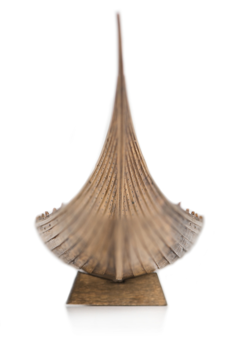 Fartygsmodell av oxelträ, rekonstruktion av "Sutton-Hooskeppet, utgrävd 1939", gravskepp daterat till ca 670 e.Kr. Skrov utfört i två halvor med limfog genom köl och stävar. Klamparna på borden pålimmade. Håarna gjorda av grankvistar med självväxt knagge. Inredning: Gångbord vid babordssidan, 19 st tofter, 8 st åror, aktra durkar, styråra med fästanordning. Skrovet betsat i tjärfärg.