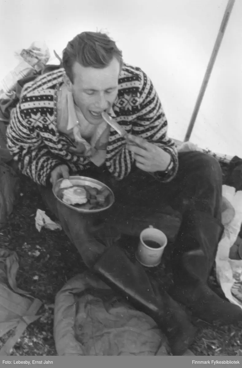 Fotografi fra tur til Peskvannet. På bildet spiser Per Bjørgan egg og bacon i teltet. Vår informant Per Bjørgan forteller at turkompisene ved Peskvannet nesten ikke hadde tid til å spise fordi de var så ivrige etter å fiske. Foto: Ernst Lebesby.