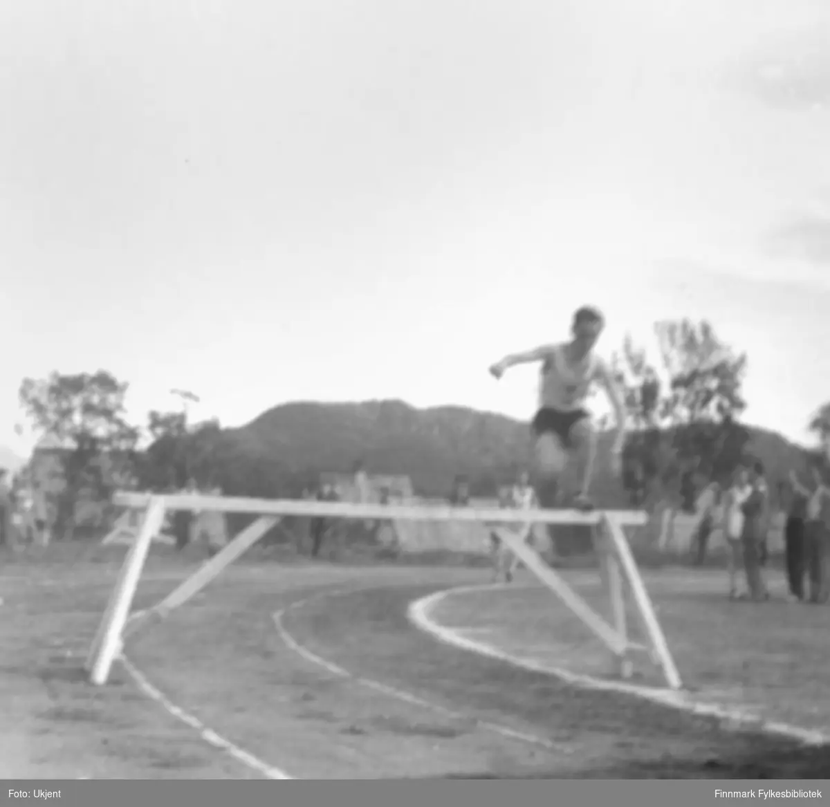 "Fra det Nord-Norske mesterskap i friidrett 1954 i Harstad. Ragnvald Dahl, Vadsø Turn,  leder stort på 3000 m. hinder. Han vant overlegent."  Foto: ukjent.