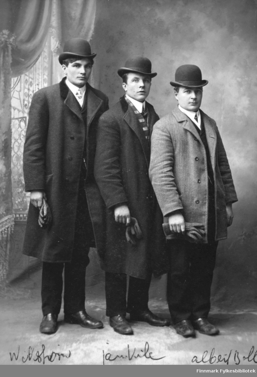 Portrett av tre unge mann. Herrene står i rad hos fotografen i Milwaukee, Usa. Alle er kledd i fine dresser med knaller og hansker. Den korteste av herrene (han til høyre) er Albert Emanuel Palo fra Vadsø som emigrerte til Michgian, Usa, i begynnelsen av 1900-tallet.