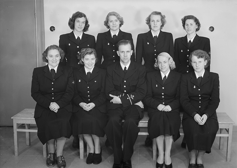 Elever och lärare vid signallottakursen på F 3 Östgöta flygflottilj, 1951. Del av klass, åtta kvinnliga elever med en manlig lärare. Grupporträtt inomhus.