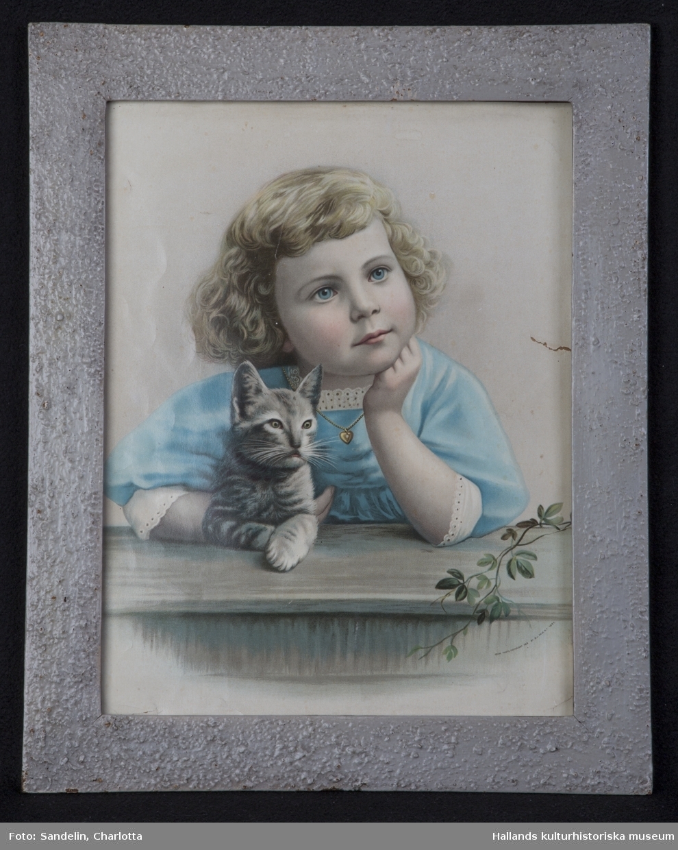 Oljetryck med ram. a) Tryck. Ung drömmande flicka med kattunge. Mått: bredd 30 cm, höjd 40 cm. b) Ram. Mått: bredd 5 cm, grå. Märkning: "FROM PHOTO. COPYRIGHT 189 BY B.J. FALK N.Y.1891".