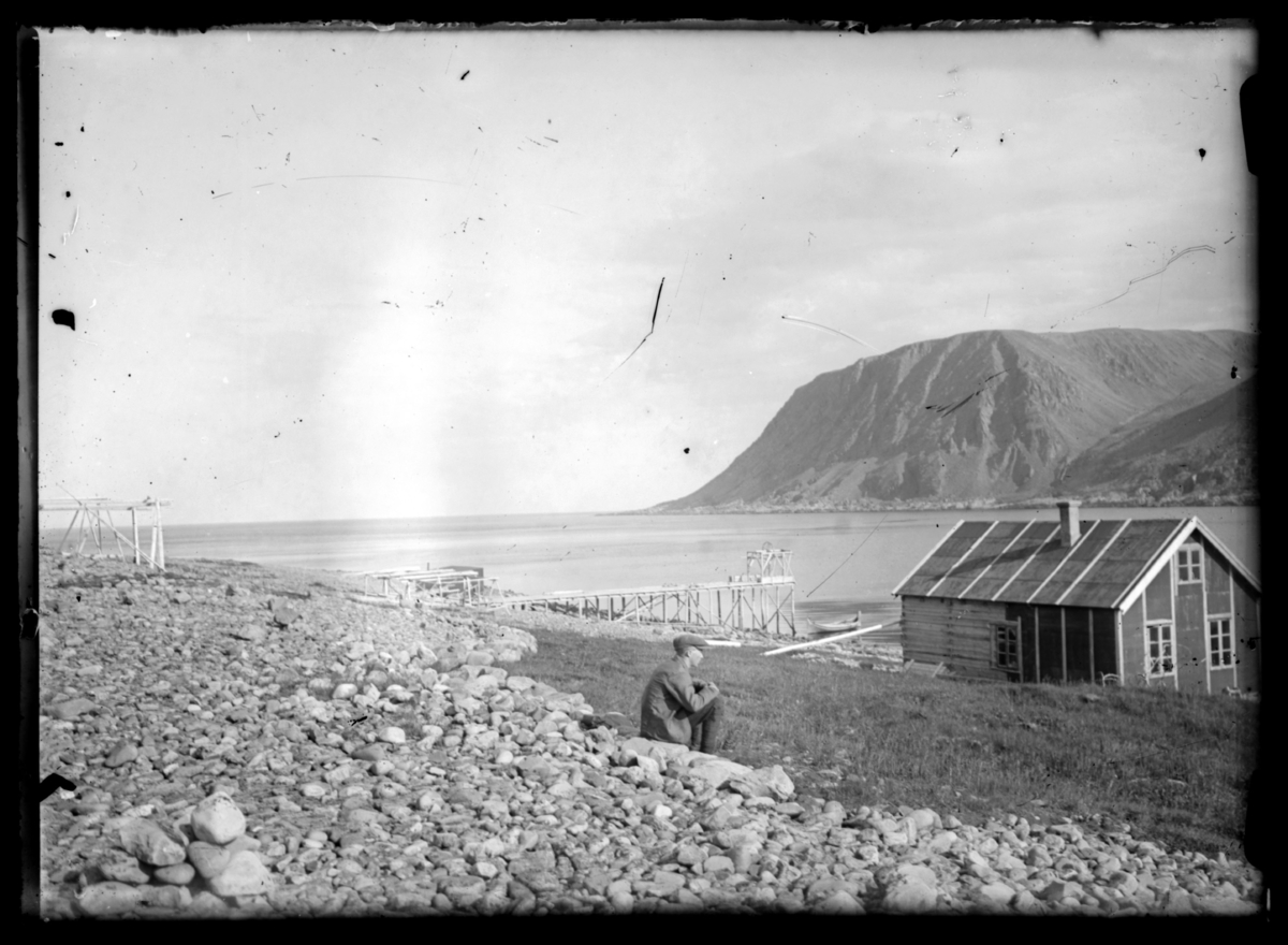 Fisker Thore Grefstad sitter på en stein i Makkaursandfjord og ser ned mot et hus og en kai ved sjøen