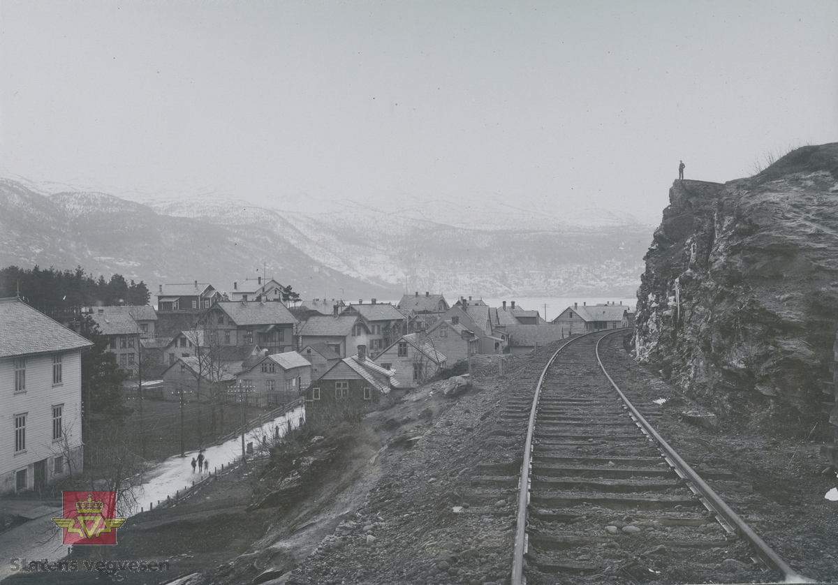 Album fra 1903-1908. Jernbanen går gjennom  et ukjent tettsted ca 1908. Et vann og snødekt  landskap i bakgrunnen.