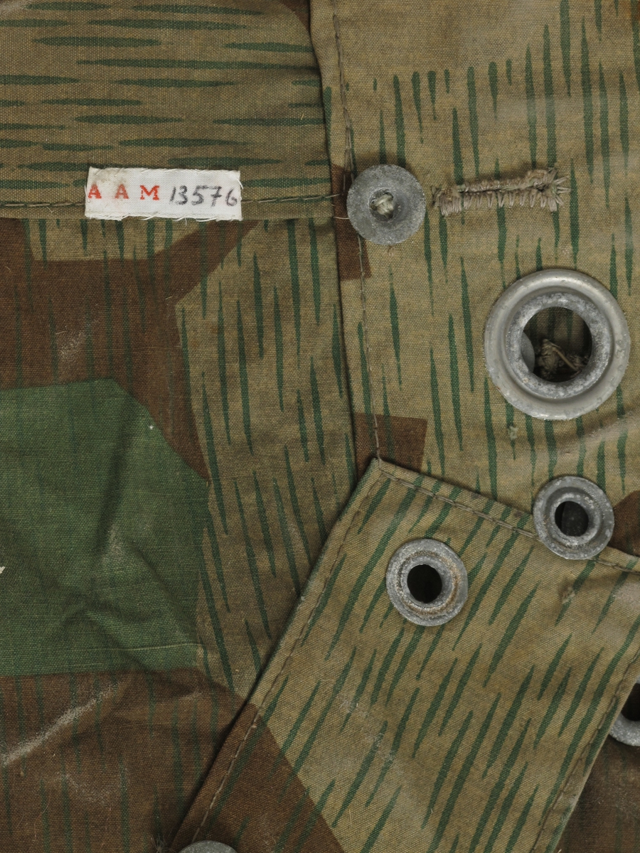 Teltduk, knappetelt, av kamuflasjestoff,  tysk, fra krigen 1940-45.  
Seilduk, lysbrunt med grønne spetter,  grønne og brune uregelmessige flekker.   
 Stort trekantet stykke stoff, med knapper  og knapphull på alle sidene,  i midtsømmen en klaff, i hjørnene ring,  i den ene ring et tau.  
Tilstand: en rift, ellers bra.